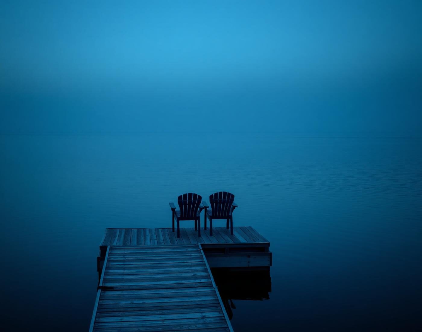 A quiet dock with two chairs facing a still bay at blue hour